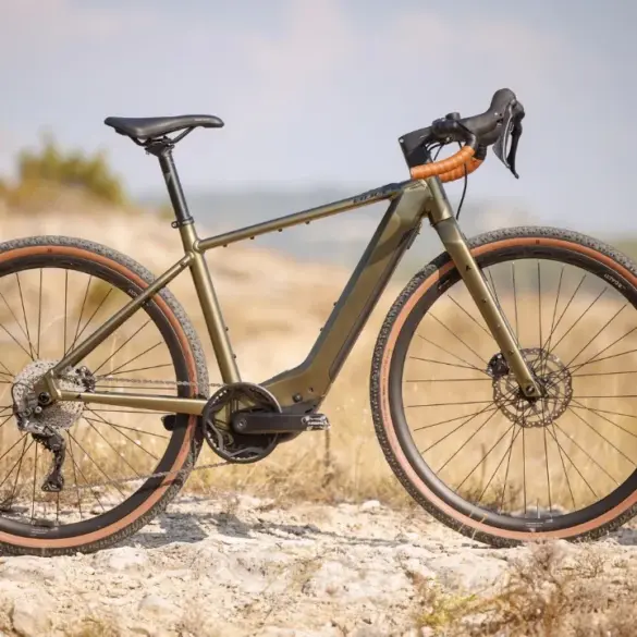 Seitenansicht eines BULLS Grinder EVO SX 2025 Diamant E-Gravelbikes in Olivgrün mit braunen Reifen auf einem Schotterweg im Freien.