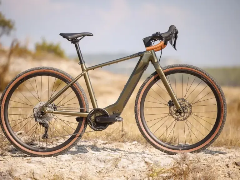 Seitenansicht eines BULLS Grinder EVO SX 2025 Diamant E-Gravelbikes in Olivgrün mit braunen Reifen auf einem Schotterweg im Freien.
