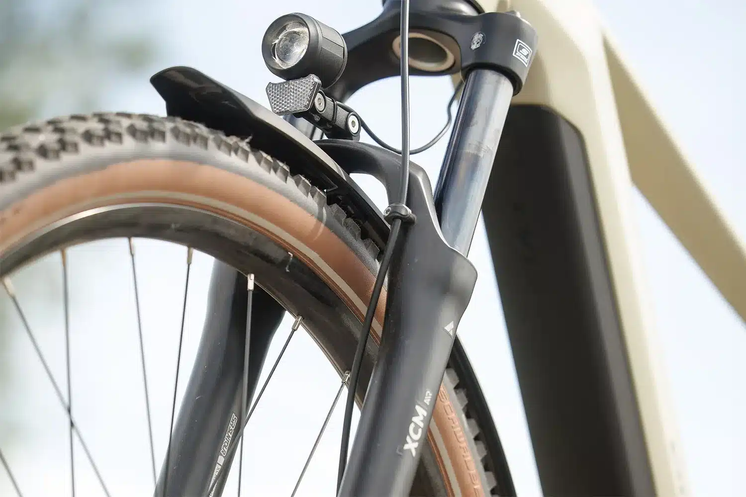 Detailansicht eines E-Bikes mit breitem Reifen, Schutzblech und integriertem Scheinwerfer.