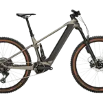 Das BULLS Sonic AM 4 ABS ist ein taupefarbenes E-Mountainbike mit Carbonrahmen und braunen Reifen, das auf einem neutralen grünen Hintergrund steht.