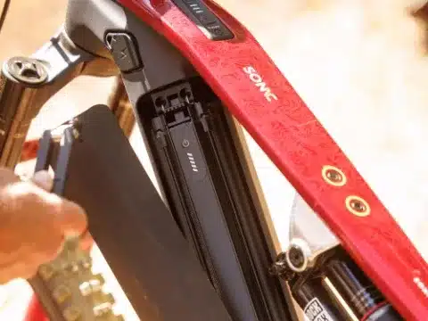 Eine Hand zieht den schwarzen Akku aus dem roten Rahmen des BULLS SONIC EN-R TEAM E-Enduro. Der Schriftzug