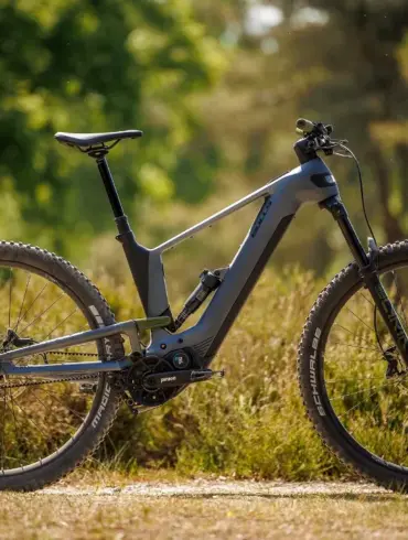 Graues E-Mountainbike Bulls Vuca EVO AM 1 mit Vollfederung und Pinion Getriebemotor, steht auf einem grasbewachsenen Untergrund im Wald.