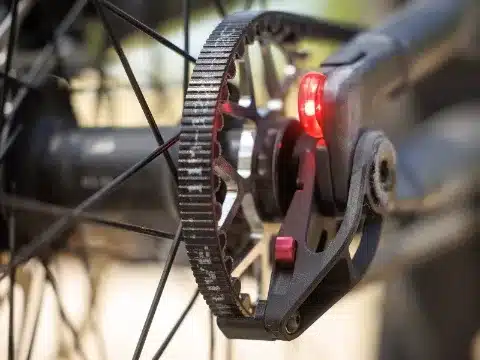 Detailaufnahme des Hinterrads und des Riemenantriebs eines E-Mountainbikes, inklusive eines roten Rücklichts.