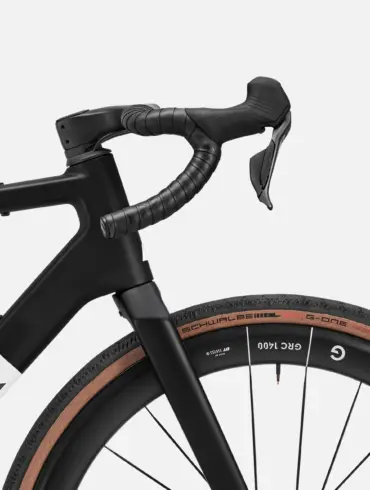 Detailansicht des Lenkers und des Vorderrads eines schwarzen Canyon Grail CF SLX 8 Di2 Gravelbikes mit braunen Reifen.