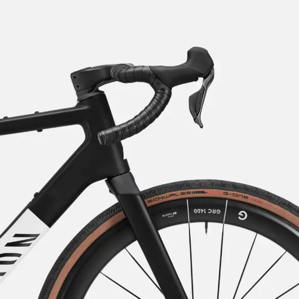 Detailansicht des Lenkers und des Vorderrads eines schwarzen Canyon Grail CF SLX 8 Di2 Gravelbikes mit braunen Reifen.