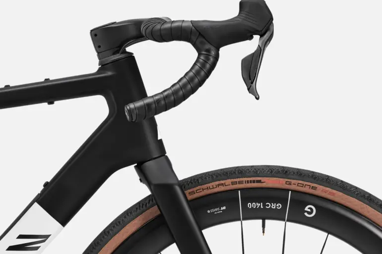 Detailansicht des Lenkers und des Vorderrads eines schwarzen Canyon Grail CF SLX 8 Di2 Gravelbikes mit braunen Reifen.