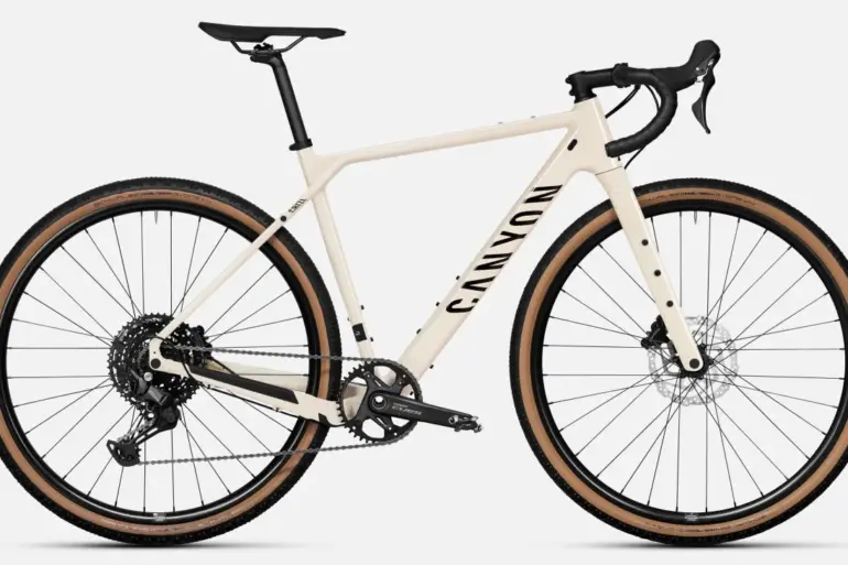 Ein sandfarbenes Canyon Grizl 5 Gravelbike von vorne, mit Fokus auf den Rahmen, die Gabel, die breiten Reifen und die Shimano Cues Schaltung.