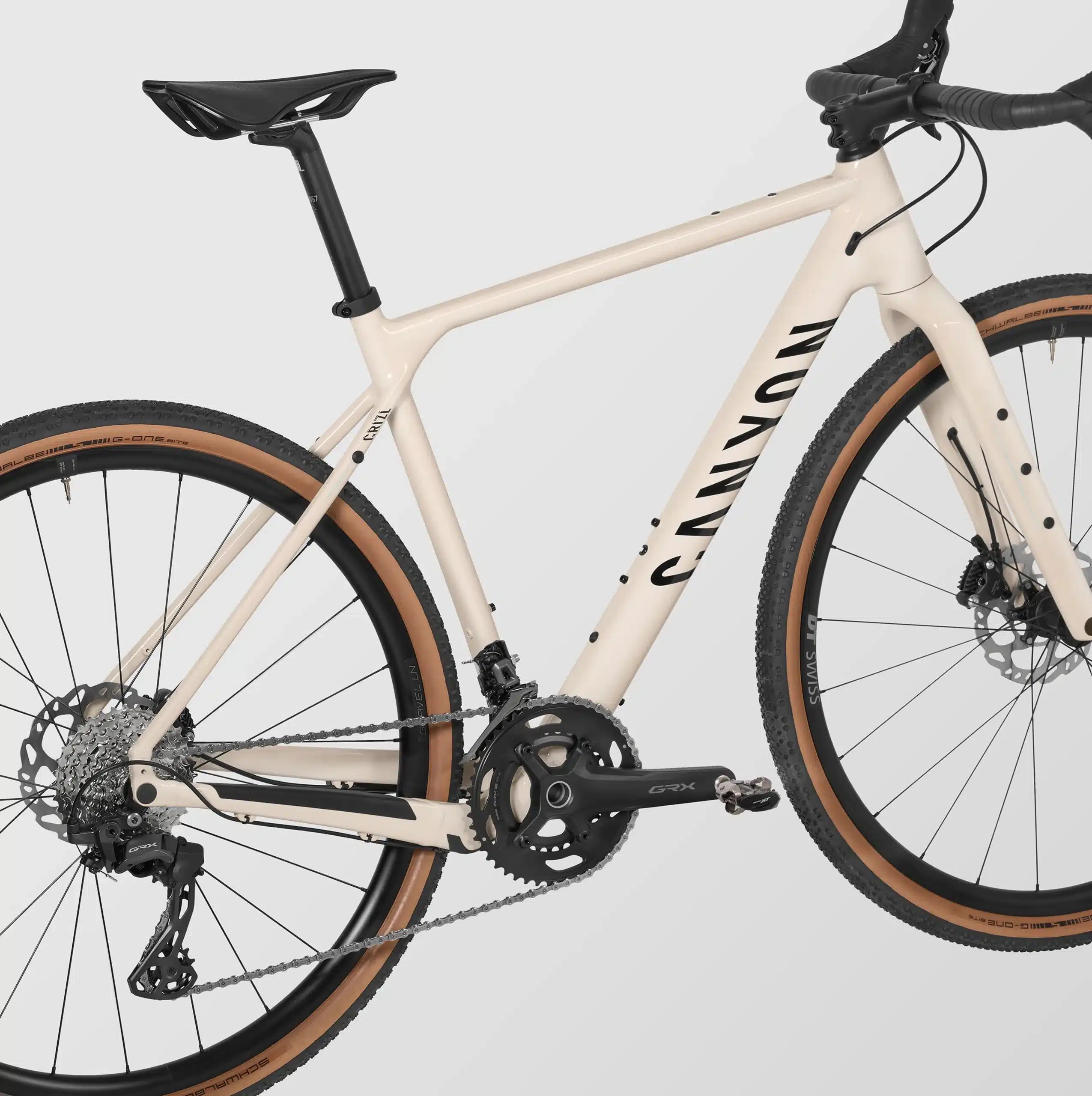 Seitenansicht eines cremefarbenen Canyon Grizl 7 Gravelbikes mit Fokus auf den Aluminiumrahmen, die Shimano GRX Kurbelgarnitur, das Schaltwerk und die DT Swiss Laufräder mit Schwalbe G-One Bite Reifen.