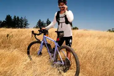 Fahrer mit Gravelbike im Sommerfeld bei Sonnenschein und blauem Himmel.