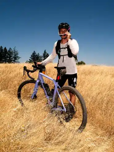 Fahrer mit Gravelbike im Sommerfeld bei Sonnenschein und blauem Himmel.