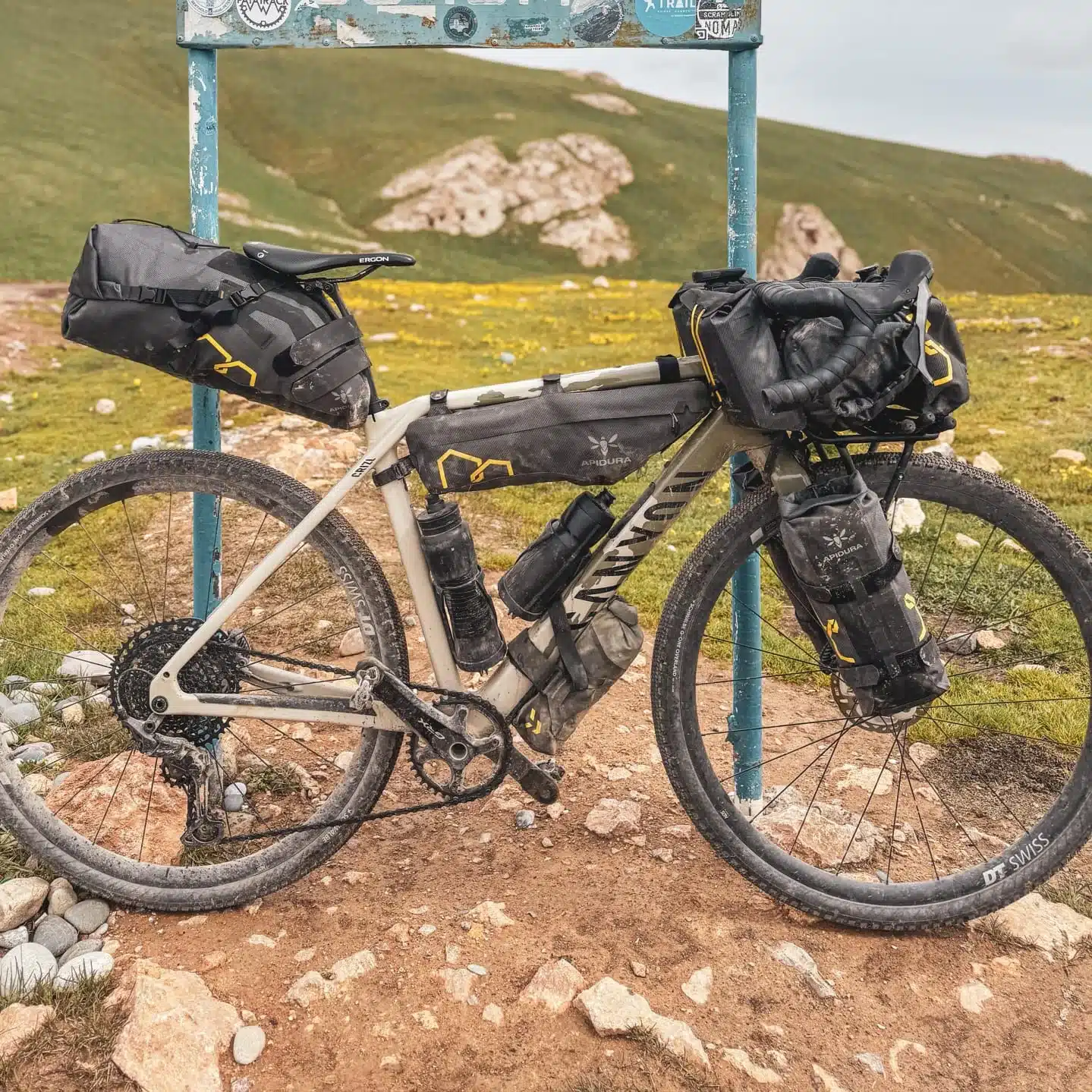 Ein Canyon Grizl CF 7 ESC Gravelbike, ausgestattet mit mehreren Bikepacking-Taschen, steht auf einem Feldweg in bergigem Gelände.