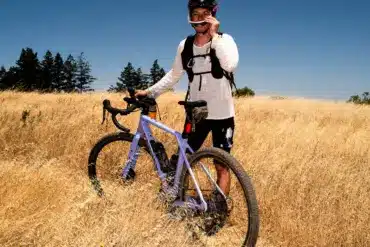 Fahrer mit Canyon Grizl CF 7 Gravelbike auf einem Feld unter blauem Himmel.