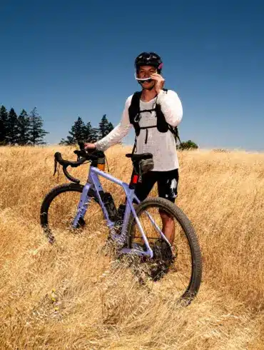 Fahrer mit Canyon Grizl CF 7 Gravelbike auf einem Feld unter blauem Himmel.