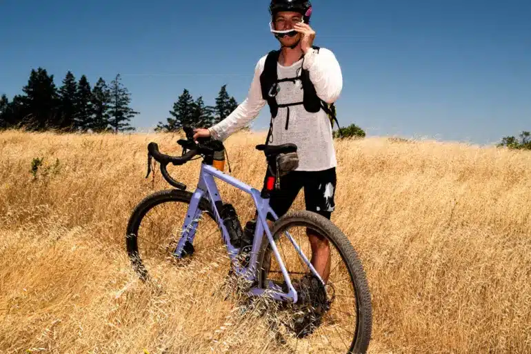 Fahrer mit Canyon Grizl CF 7 Gravelbike auf einem Feld unter blauem Himmel.