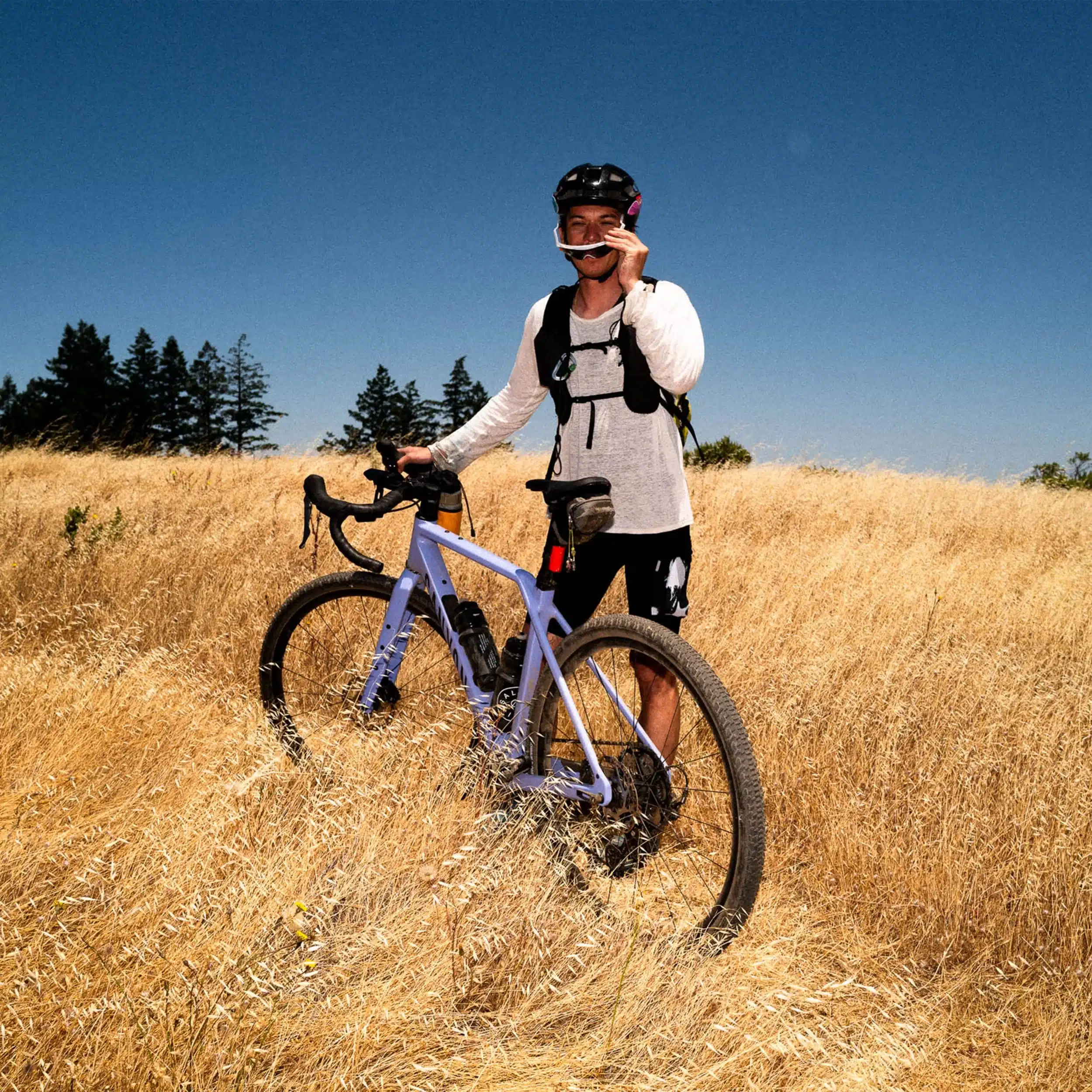 Fahrer mit Canyon Grizl CF 7 Gravelbike auf einem Feld unter blauem Himmel.
