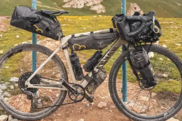 Ein Canyon Grizl CF 9 ESC w/ RIFT Gravelbike ist auf einem Feldweg abgestellt, voll beladen mit Bikepacking-Taschen, vor einer hügeligen Landschaft.