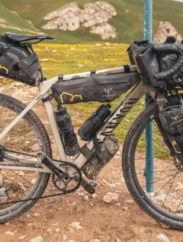 Ein Canyon Grizl CF 9 ESC w/ RIFT Gravelbike ist auf einem Feldweg abgestellt, voll beladen mit Bikepacking-Taschen, vor einer hügeligen Landschaft.
