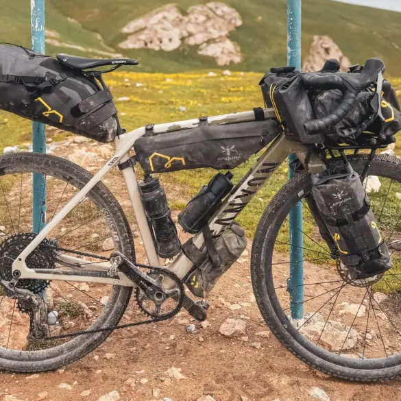 Ein Canyon Grizl CF 9 ESC w/ RIFT Gravelbike ist auf einem Feldweg abgestellt, voll beladen mit Bikepacking-Taschen, vor einer hügeligen Landschaft.