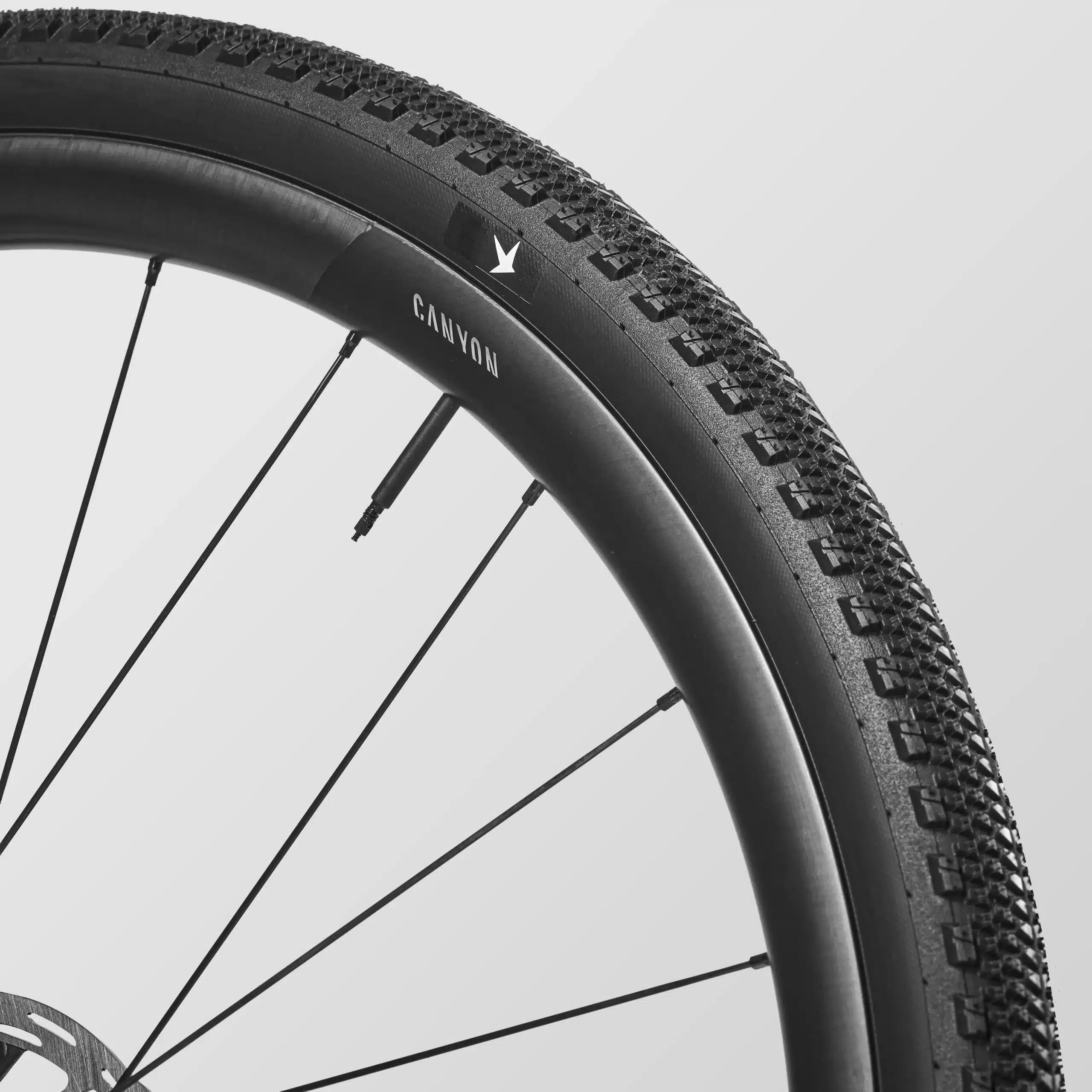 Nahaufnahme eines Fahrradlaufrads des Canyon Grizl CF 9 ESC w/ RIFT, das eine schwarze Canyon-Felge und einen schwarzen Gravelreifen mit ausgeprägtem Profil zeigt.