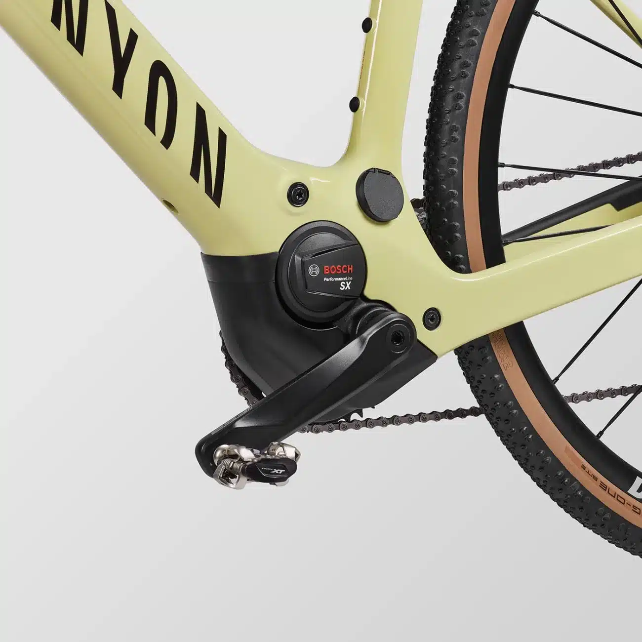 Nahaufnahme des Tretlagerbereichs eines hellgelben Canyon Grizl:ONfly CF 7 E-Gravelbikes mit sichtbarem Bosch Performance Line SX Motor, Kurbel und Pedal.