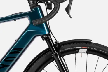 Detailansicht eines Canyon Grizl:ONfly CF Daily E-Gravelbikes, das den blauen Carbonrahmen, die Shimano Schaltgriffe, den vorderen Reifen mit Schwalbe G-One Overland Schriftzug und ein schwarzes Schutzblech zeigt.
