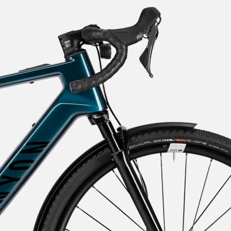 Detailansicht eines Canyon Grizl:ONfly CF Daily E-Gravelbikes, das den blauen Carbonrahmen, die Shimano Schaltgriffe, den vorderen Reifen mit Schwalbe G-One Overland Schriftzug und ein schwarzes Schutzblech zeigt.