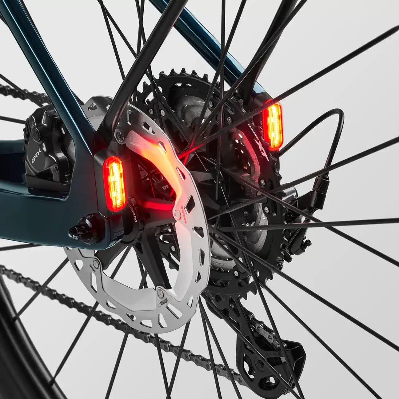 Detailbild der Hinterradnabe eines Canyon Grizl:ONfly CF Daily E-Gravelbikes mit integrierten roten Rückleuchten, Disc-Bremse und Shimano GRX Schaltwerk.