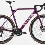 Das Canyon Inflite CFR ist ein Cyclocross-Rennrad mit einem lila-violetten Carbonrahmen, weißen Canyon-Aufschriften auf dem Unterrohr und Schriftzug 'INFLITE' am Sitzrohr. Es verfügt über eine elektronische Shimano Dura-Ace Schaltung, Rotor Aldhu Kurbel mit Leistungsmesser und DT Swiss CRC 1100 Carbon-Laufräder mit Schwalbe X-One Reifen.