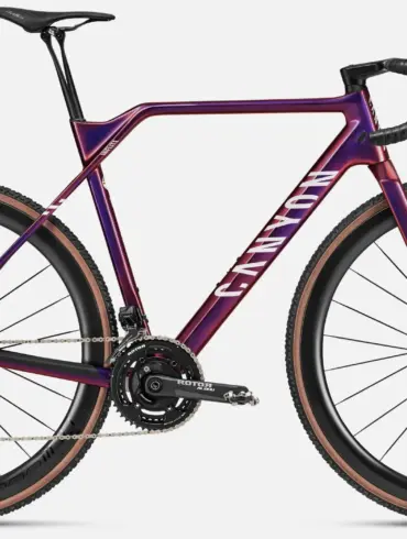 Das Canyon Inflite CFR ist ein Cyclocross-Rennrad mit einem lila-violetten Carbonrahmen, weißen Canyon-Aufschriften auf dem Unterrohr und Schriftzug 'INFLITE' am Sitzrohr. Es verfügt über eine elektronische Shimano Dura-Ace Schaltung, Rotor Aldhu Kurbel mit Leistungsmesser und DT Swiss CRC 1100 Carbon-Laufräder mit Schwalbe X-One Reifen.