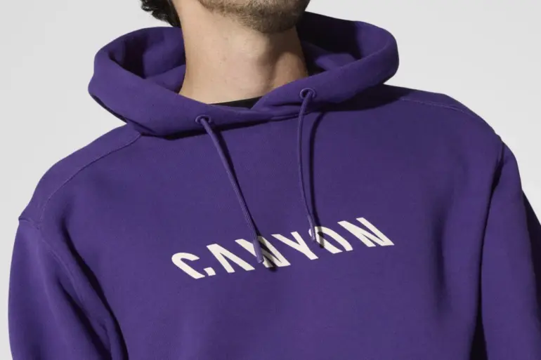 Ein Mann trägt einen lilafarbenen Canyon Men’s Hoodie mit weißem "CANYON"-Schriftzug auf der Brust.