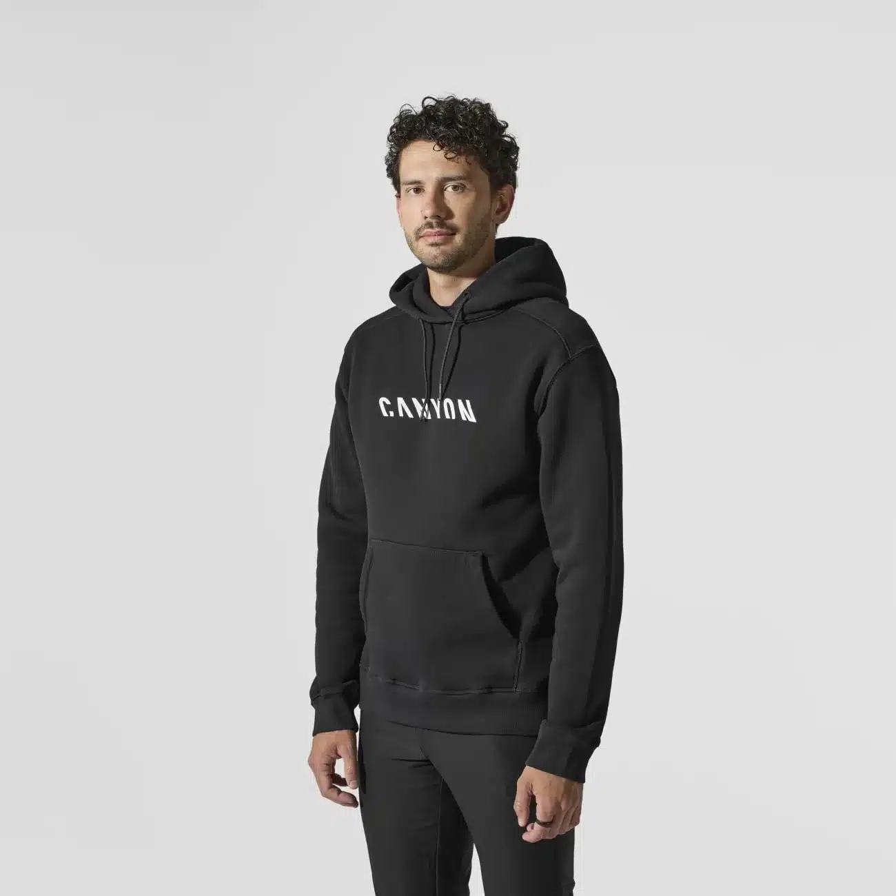 Ein Mann steht in einem schwarzen Hoodie mit dem weißen Schriftzug