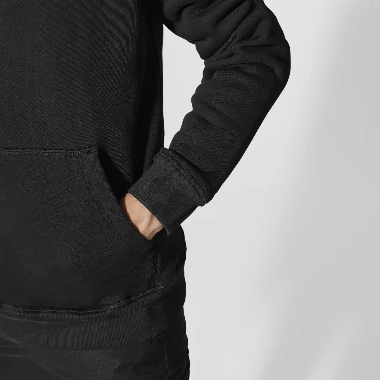 Person steckt die Hand in die Kängurutasche eines schwarzen Canyon Men's Hoodies.
