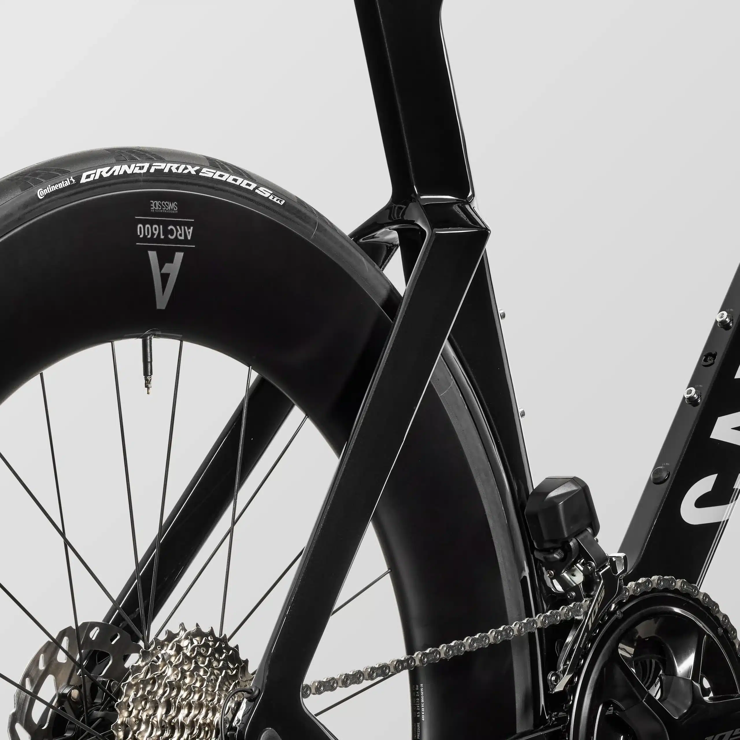 Detailaufnahme eines schwarzen Triathlonrads, Fokus auf das Hinterrad mit Carbonfelge, Kette, Kassette und Schaltwerk, sowie den aero-dynamisch geformten Carbonrahmen.