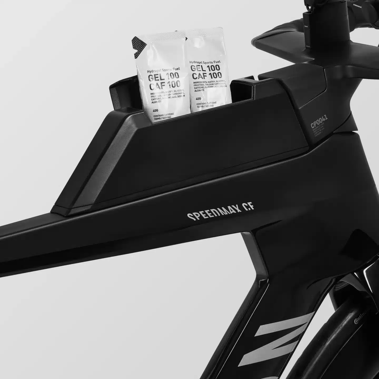 Nahaufnahme des vorderen Rahmenteils eines schwarzen Canyon Speedmax CF 8 Di2 Race Triathlonrads, auf dem zwei Energie-Gels mit der Beschriftung 'Hydrogel Sports Fuel GEL 100 CAF 100' in einem integrierten Fach platziert sind.