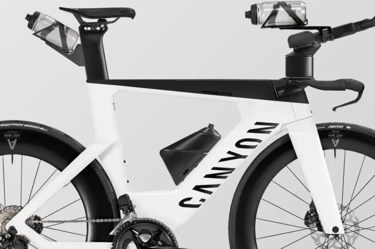 Seitenansicht eines weißen Canyon Speedmax CF SLX 7 Di2 Triathlonrads mit integrierten Trinkflaschen und Aero-Aufsätzen.