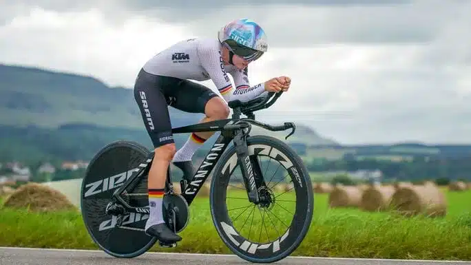 Radsportler fährt Canyon Speedmax CFR TT Zeitfahrrad auf einer Straße mit Feldern und Heuballen im Hintergrund.
