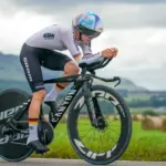 Eine Rennfahrerin auf einem Canyon Speedmax CFR TT Zeitfahrrad, in voller Fahrt auf einer asphaltierten Straße im ländlichen Raum.