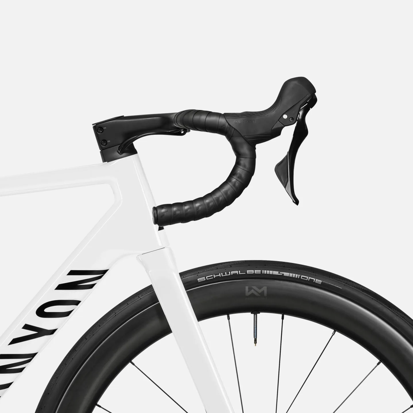 Nahaufnahme des weißen Rahmens, des schwarzen Carbon-Cockpits und der Shimano 105 Schalthebel eines Canyon Ultimate CF 7 A.50 Rennrads, mit Sicht auf das Vorderrad mit Schwalbe Reifen.
