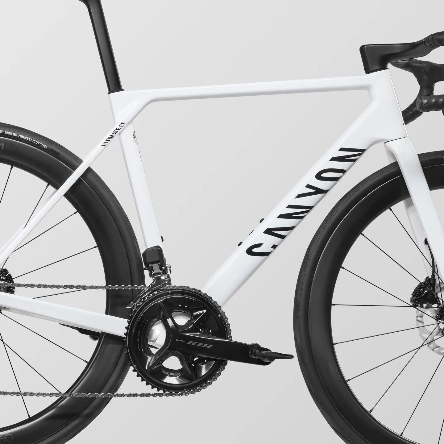 Nahaufnahme des weißen Canyon Ultimate CF 7 Di2 Rennrads mit Blick auf den Schriftzug 'CANYON' am Unterrohr, die Shimano 105 Kurbel und die Carbonlaufräder.