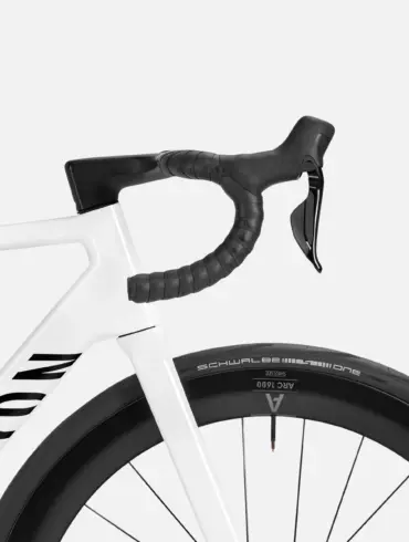 Detailaufnahme eines weißen Canyon Ultimate CF 7 Di2 Aero Rennrads mit Fokus auf das integrierte schwarze Cockpit und das Vorderrad mit Carbonfelge und Schwalbe Reifen.