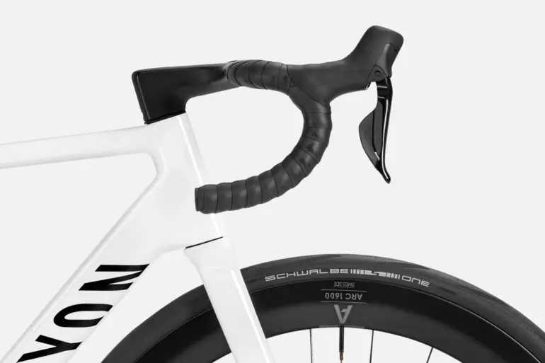 Detailaufnahme eines weißen Canyon Ultimate CF 7 Di2 Aero Rennrads mit Fokus auf das integrierte schwarze Cockpit und das Vorderrad mit Carbonfelge und Schwalbe Reifen.