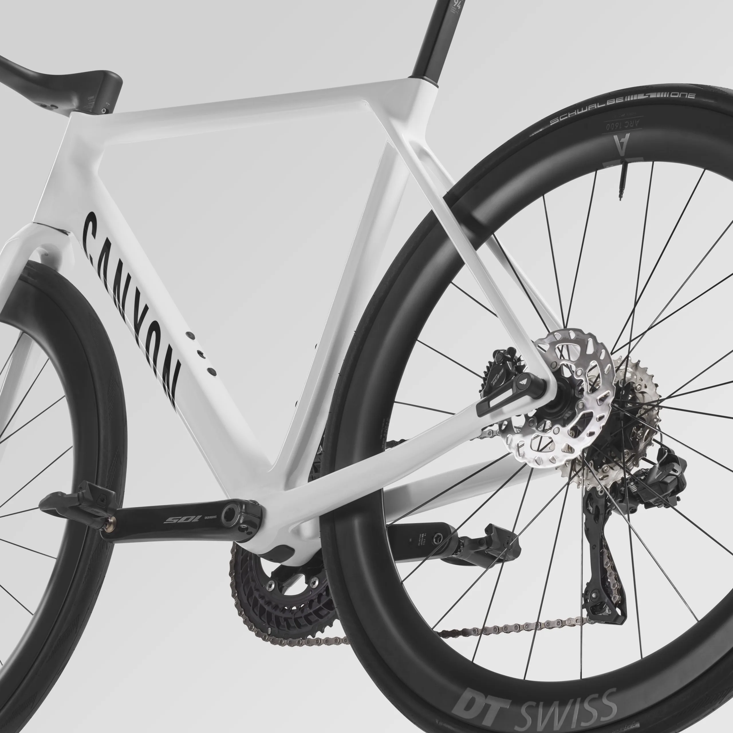 Detailaufnahme des Hinterrads eines weißen Canyon Ultimate CF 7 Di2 Aero Rennrads mit Fokus auf die DT Swiss ARC Carbonfelge, die Schwalbe One Bereifung, die Shimano 105 Di2 Schaltung und die Kette.