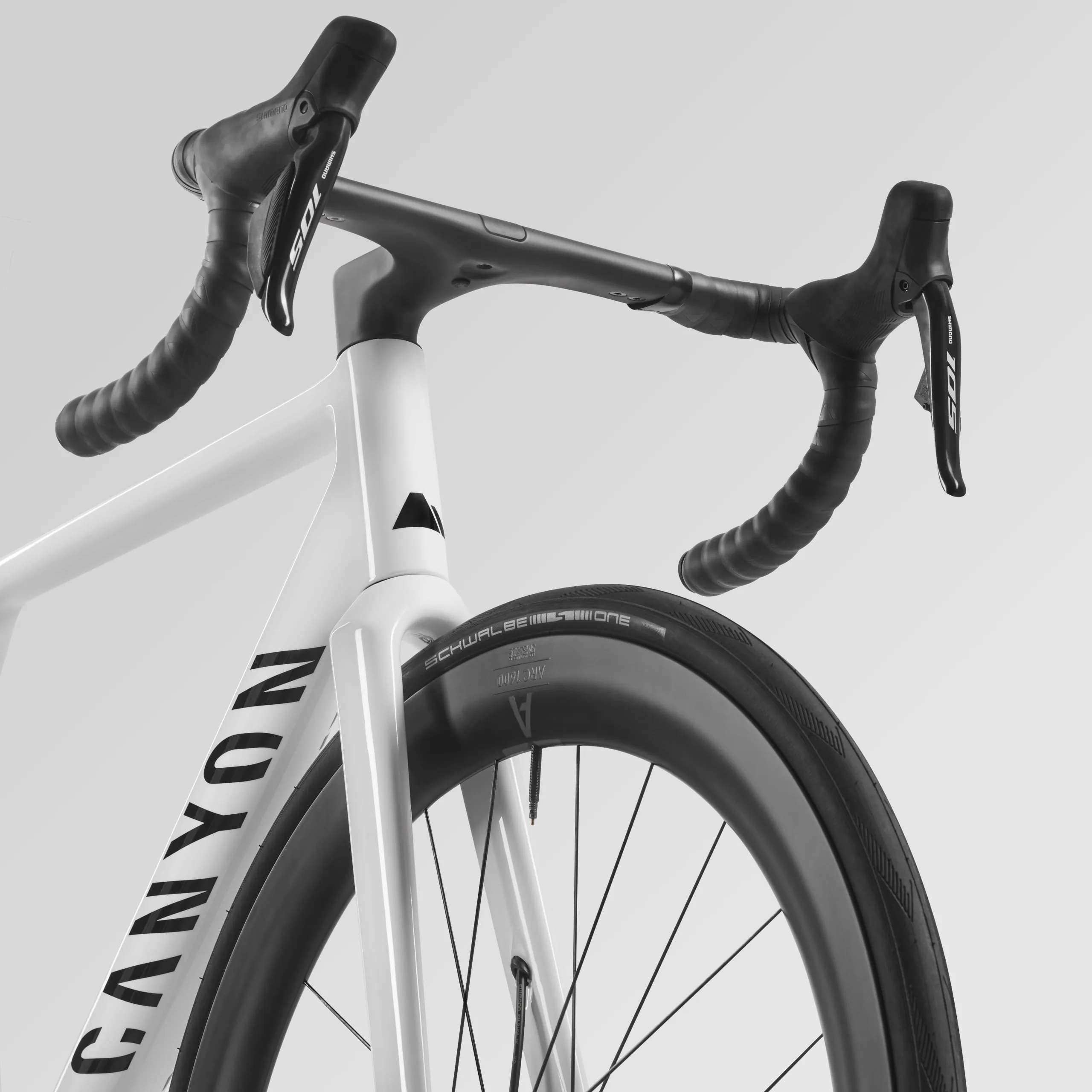 Detailaufnahme eines weißen Canyon Ultimate CF 7 Di2 Aero Rennrads, Fokus auf das integrierte Carbon-Cockpit und das Vorderrad mit Schwalbe Reifen.