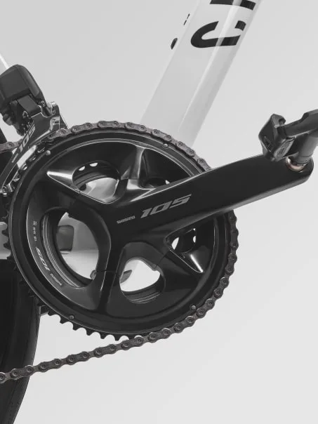 Detailaufnahme der Shimano 105 Kurbelgarnitur mit Kette und vorderem Schaltwerk an einem weißen Rennrad.