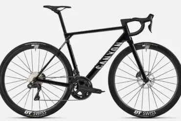 Seitenansicht eines schwarzen Canyon Ultimate CF SLX 8 Di2 Rennrads mit DT Swiss Carbon-Laufrädern und Shimano Ultegra Di2 Schaltung auf grauem Hintergrund.