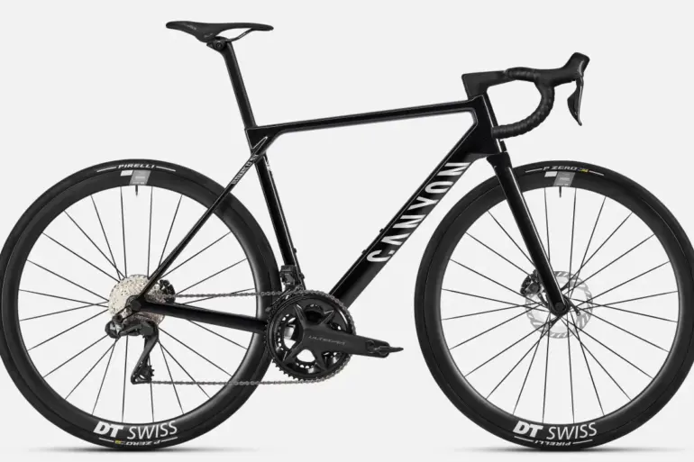 Seitenansicht eines schwarzen Canyon Ultimate CF SLX 8 Di2 Rennrads mit DT Swiss Carbon-Laufrädern und Shimano Ultegra Di2 Schaltung auf grauem Hintergrund.