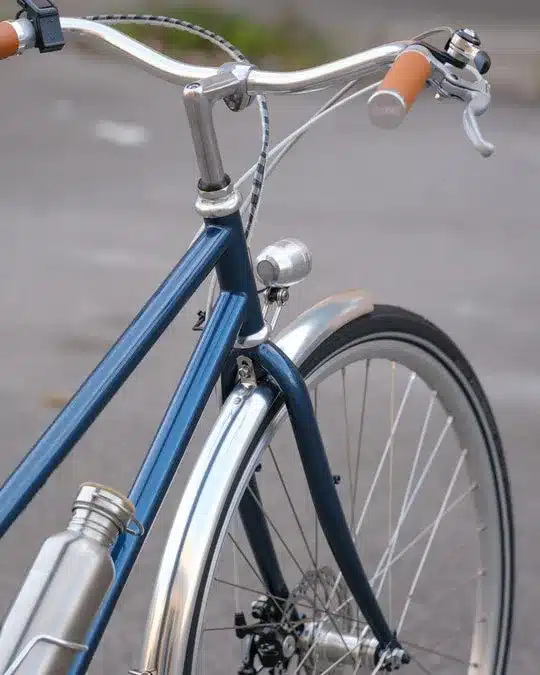 Vorderrad und obere Rahmenpartie eines blauen Capri Azur 4 E-Bikes mit silbernen Schutzblechen und braunen Griffen.
