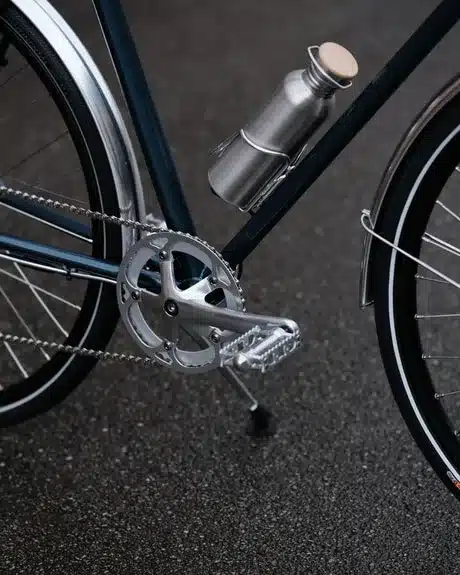 Nahaufnahme des silbernen Kurbelbereichs und der Pedale eines dunkelblauen Capri Azur 4 E-Bikes mit montierter silberner Trinkflasche in einem Halter.