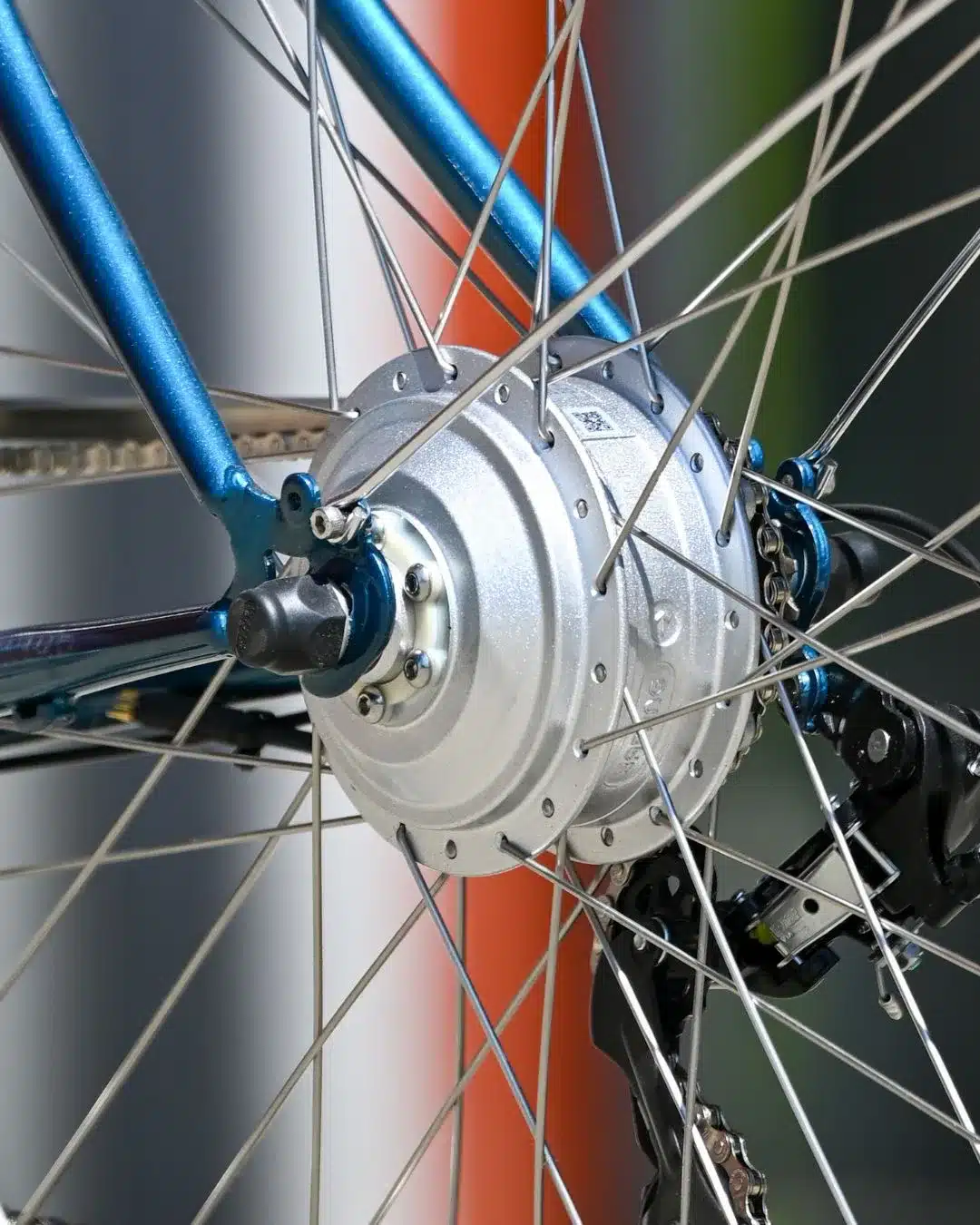 Nahaufnahme des silbernen Nabenmotors am Hinterrad eines blauen Capri Berlin Electric 3 Fahrrads, mit Speichen und Teilen des Rahmens sichtbar.