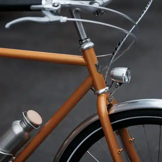 Detailaufnahme eines orangefarbenen Capri Metz E-Bikes mit Fokus auf den vorderen Rahmenbereich, Lenker und einem montierten Trinkflaschenhalter.